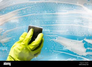 persona limpiando ventana con guantes y esponja